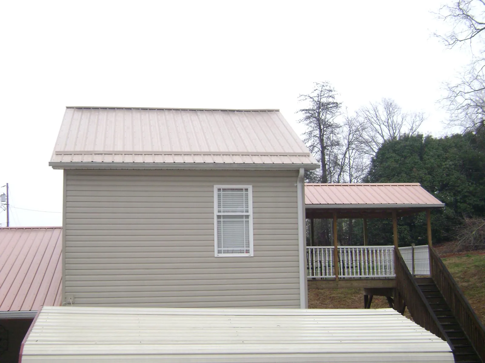 Tan metal roofs on a two story addition and attached porch, from a Roof Replacement job in Brunswick
